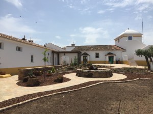 The main building is white with a tiled roof and golden yellow painted base. The landscaping in the foreground has been recently planted and includes a tile walkway with a round sitting bench.